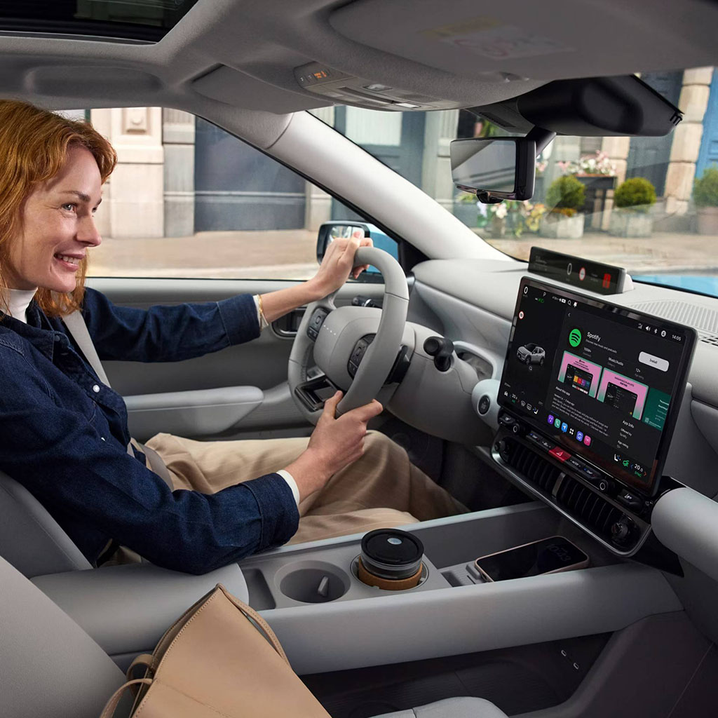 IONIQ 3 sisätila, nainen ratin takana, näytöllä PLEOS App Market
