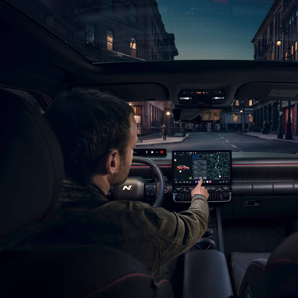 Hyundai IONIQ 3 sisäkuva, mies asettaa navigoinnin kohdetta pimeällä kaupungin kadulla