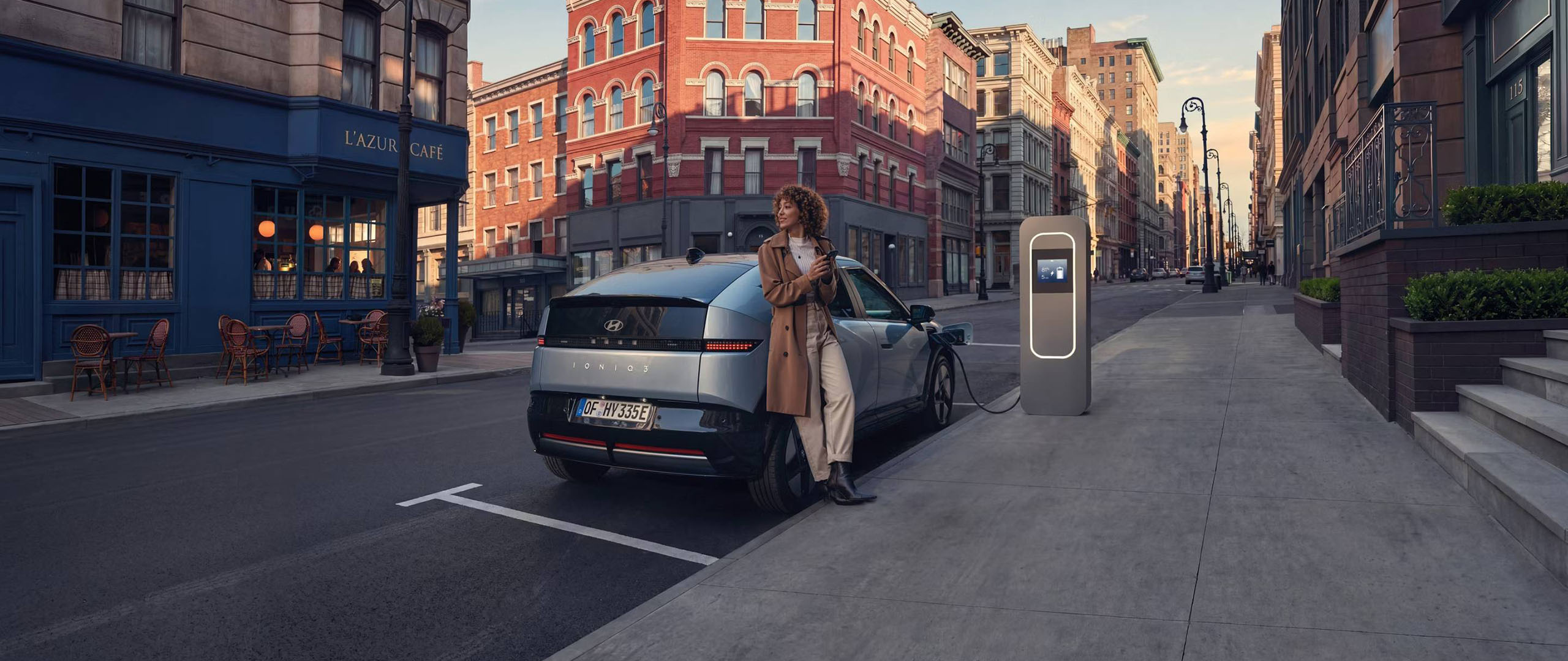 Hyundai IONIQ 3 on latauksessa kadunvarsipaikalla kaupungissa, nainen odottelee vieressä