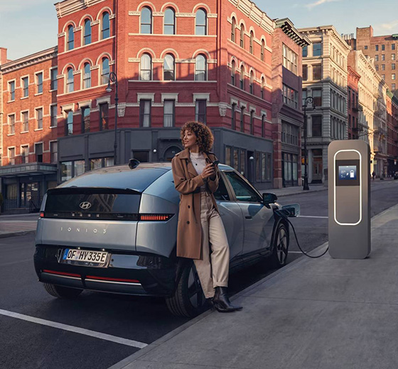 Hyundai IONIQ 3 on latauksessa kadunvarsipaikalla kaupungissa, nainen odottelee vieressä