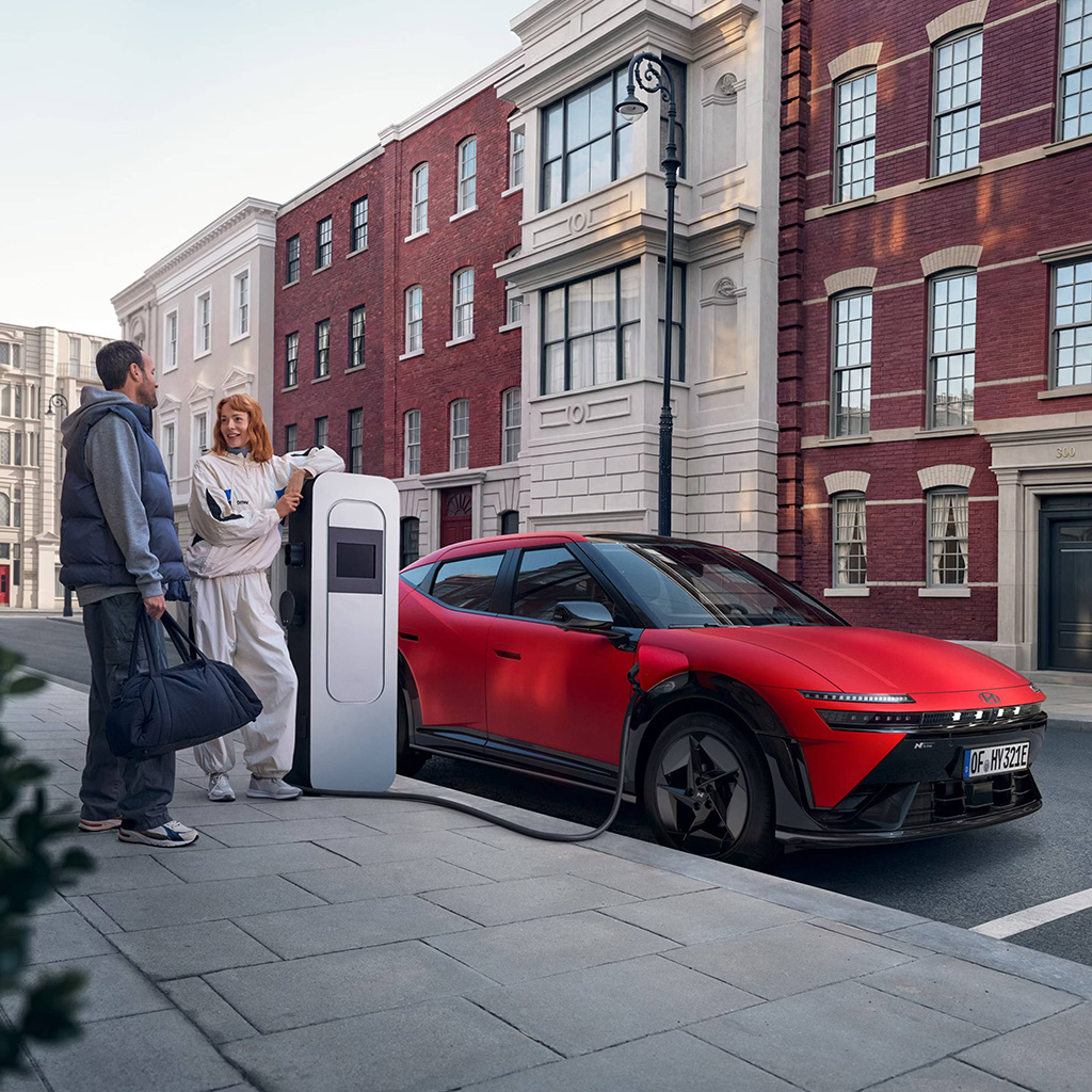 Hyundai IONIQ 3 N Line latauksessa kadunvarsipaikalla kaupungissa, pariskunta odottelee vieressä.